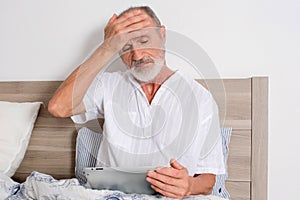 Elderly man with headache in bed looking for a doctor