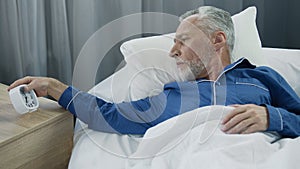 Elderly man hearing alarm clock, reluctant to wake up, lack of sleep and energy