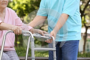 Elderly man helping his wife with walking frame outdoors