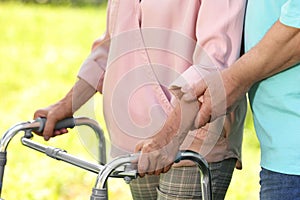 Elderly man helping his wife with walking frame outdoors