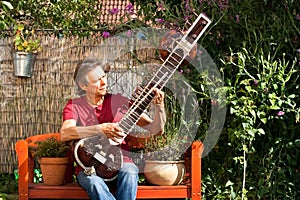 Elderly man in his garden is playing a sitar