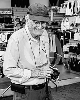 Elderly man holding a digital camera in his hand while smiling for the camera.
