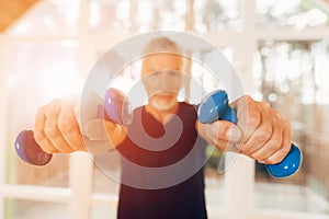 An elderly man is holding dumbbells in his hands in a nursing home.