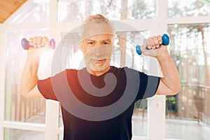 An elderly man is holding dumbbells in his hands in a nursing home.