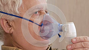 An elderly man holding a mask from an inhaler at home. Treats inflammation of the airways via nebulizer. Preventing