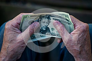 Elderly man holding US dollar bills in hands, 20 dollar note in pensioner hand