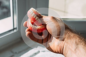 An elderly man holds a denture. A man is holding dentures in his hands. Removable dentures flexible. False teeth. Implant.