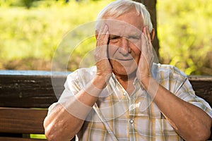 Elderly man holds his head.