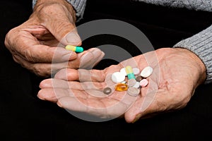 An elderly man holds a lot of colored pills in old hands