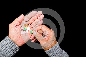 An elderly man holds many colored pills in old hands on a dark background. Painful old age. Health care for the elderly.  The View