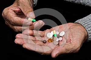 An elderly man holds a lot of colored pills in old hands. Painful old age. Health care of older people