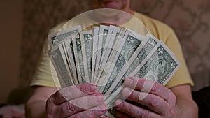 An elderly man holds a pack of one-dollar bills in his hands