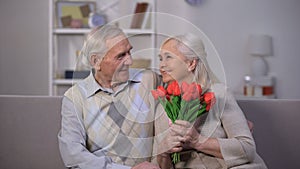 Elderly man hugging happy woman with bunch of tulips, present from beloved