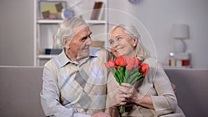 Elderly man hugging happy woman with bunch tulips, present greeting, attention