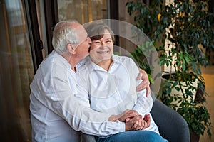 An elderly man hugs and kisses hss smiling wife