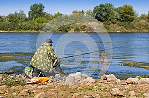 An elderly man in a jacket, baseball cap and rubber boots fishin