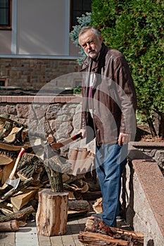 Elderly man in jacket stands in front of pile firewood