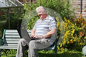 An elderly man with laptop outside.