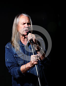 Elderly man with long gray hair sings into a microphone