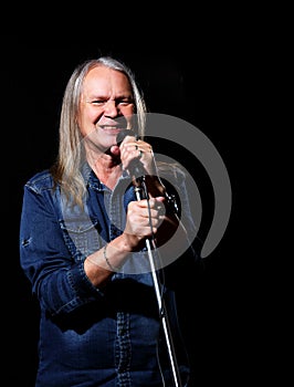 Elderly man with long gray hair sings into a microphone