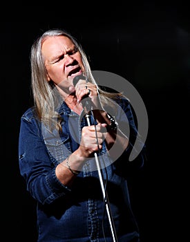 Elderly man with long gray hair sings into a microphone