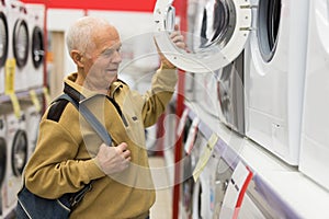 Elderly man looks at the washing machine on the counter