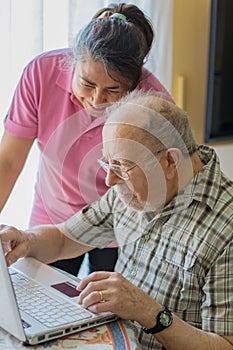 Elderly man looks and writes to the computer helped by his caregiver