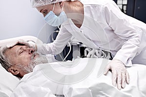 elderly man lying on bed suffering from disease, female nurse checking the temperature