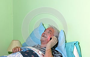 Elderly or senior man lying in  bed and using cell phone