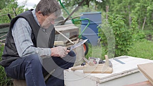 An elderly man makes a wooden box at the cottage in the summer