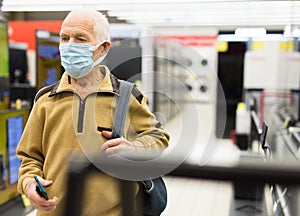 Elderly man in medical mask looking TV in showroom of electronics store