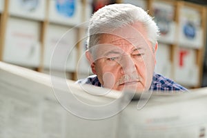 Elderly man with mustache reading paper in library