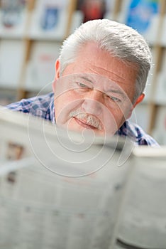 Elderly man with mustache reading paper in library