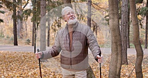 elderly man with nordic walking sticks looks up, enjoys the beauty of golden season