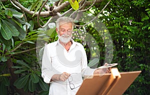 Elderly man painting something on a canvas in ther park happliy.Painting Concept,Lifestyle concept,Creative concept.