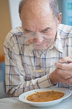 Elderly man with Parkinsons disease holds spoon in both hands