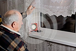 Elderly man peering out through the window