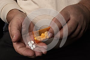 Elderly man with pills and orange pill bottle in hands at home