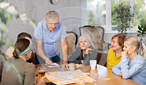 Elderly man playing board game during tea party with friends