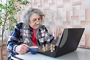An elderly man playing chess at home on the computer