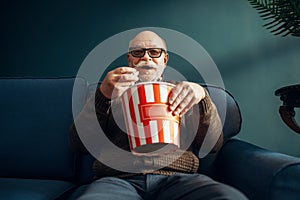 Elderly man with popcorn watching TV on couch