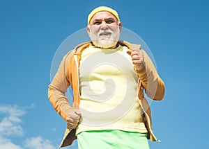 Elderly man practicing sports on blue sky background. Elderly man jogging. Golden age grandfather. Senior fitness person