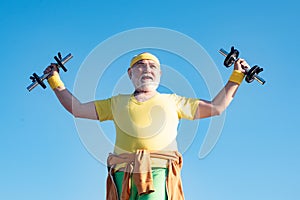 Elderly man practicing sports on blue sky background. Senior man lifting weights. Health for aged pensioner. Senior