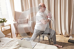 Elderly man practicing yoga asana warrior using chair