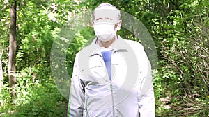 An elderly man in a protective mask walks in the Park, a walk in the fresh air after quarantine, a precautionary measure
