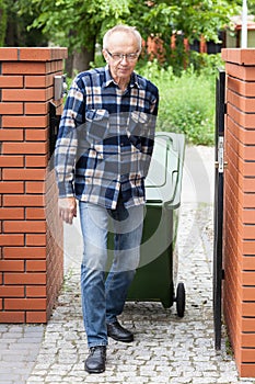 Elderly man pulling a wheeled dumpster