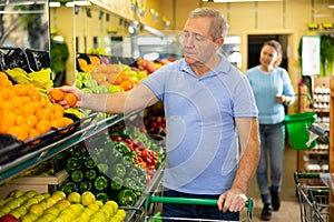 Elderly man purchaser taking fresh tangerines in grocery store