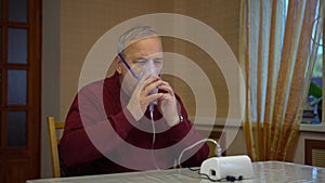 An elderly man puts on an inhaler mask. A man does a respiratory procedure at home.