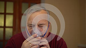 An elderly man puts on an inhaler mask. A man does a respiratory procedure at home. Closeup.