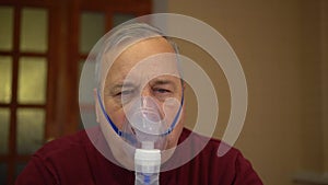 An elderly man puts on an inhaler mask. A man does a respiratory procedure at home. Closeup.